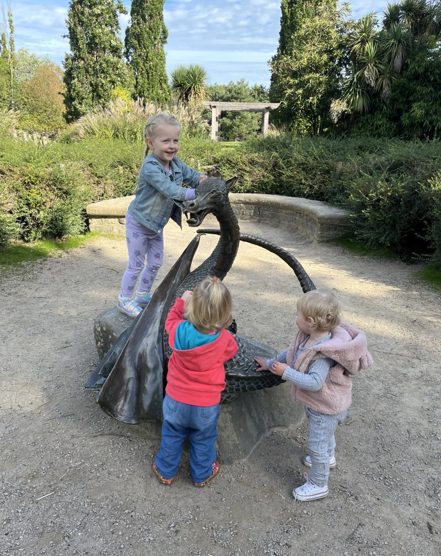 Three children standing on, and next to, the Dragon sculptire